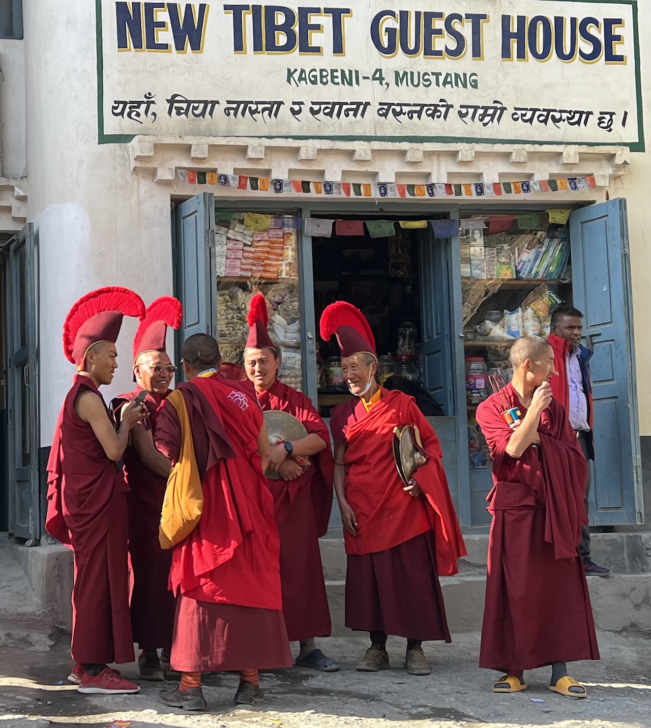 Monaci tibetani in tuniche rosse e cappelli alti davanti all'insegna "NEW TIBET GUEST HOUSE" a Kagbeni.