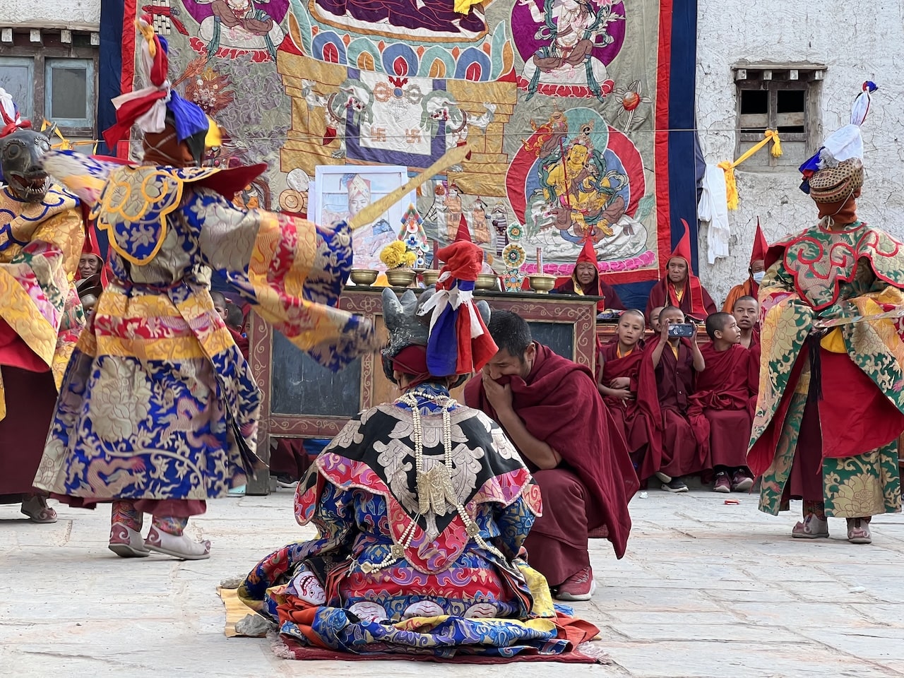 Danzatori mascherati in costumi tradizionali colorati e monaci in tuniche rosse durante una cerimonia rituale.