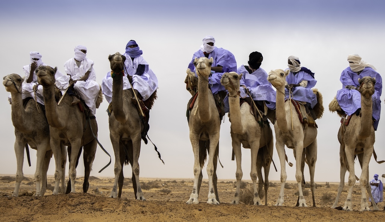 Uomini vestiti con abiti tradizionali e turbanti bianchi e blu cavalcano dromedari nel deserto