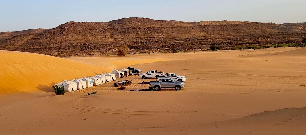 Accampamento turistico nel deserto della Mauritania, con tende e fuoristrada, ai piedi di una duna.