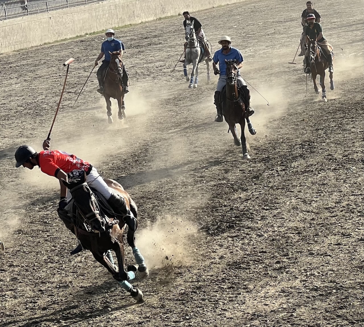 Scena dinamica di una partita di polo; cavalieri con mazze su cavalli galoppano sollevando polvere sull'arena