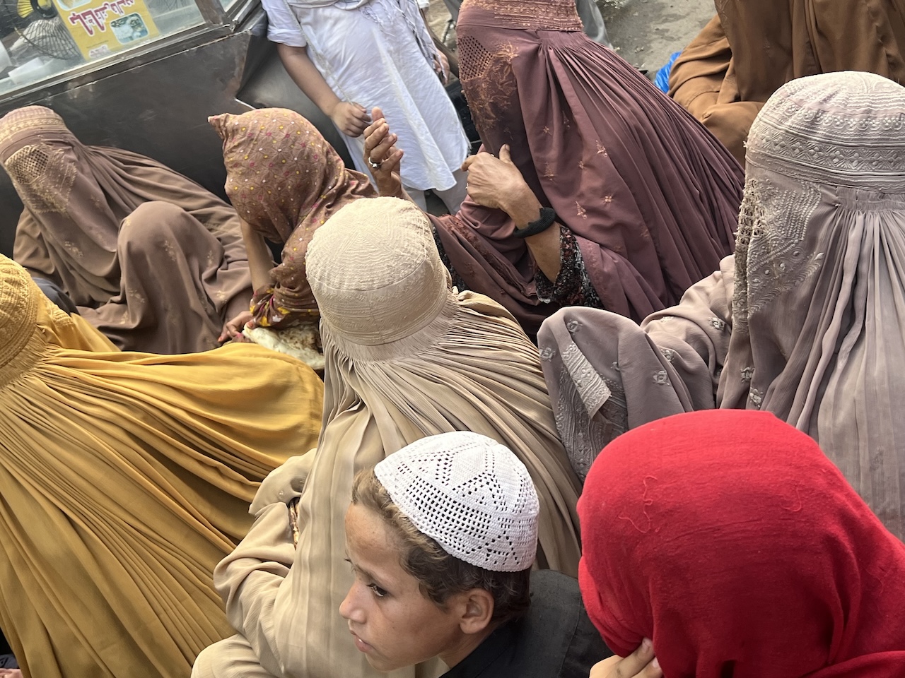 Primo piano di un bambino con un cappello lavorato a maglia tra donne con burqa color terra in una folla a Peshawar.