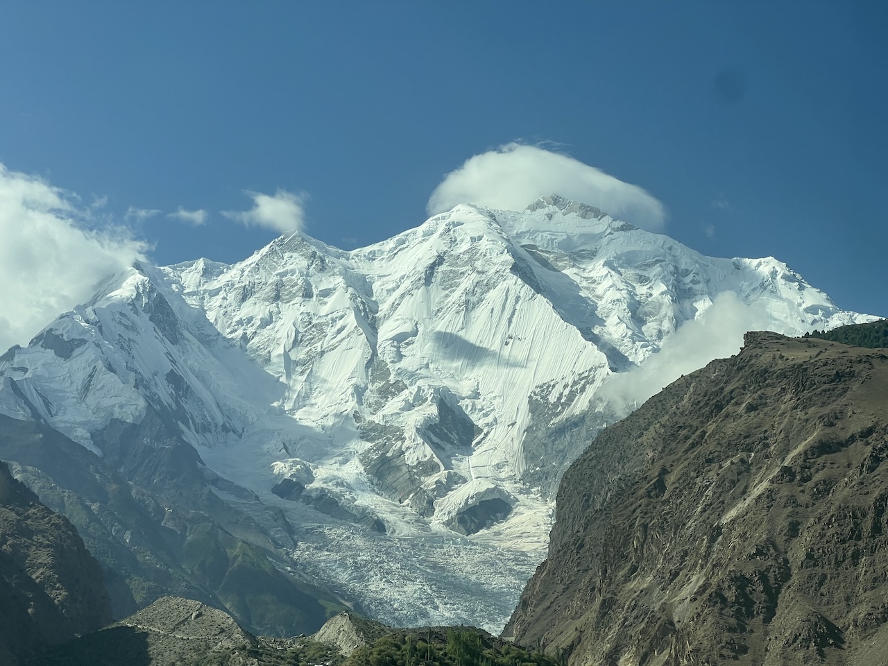 Enorme montagna innevata con un ghiacciaio visibile, una vetta molto alta, circondata da cime e vallate rocciose