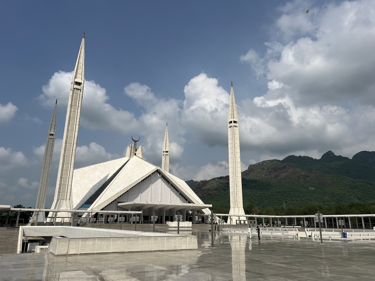 Vasta e moderna Moschea Shah Faisal a Islamabad con quattro minareti e sfondo di colline verdi sotto il cielo azzurro