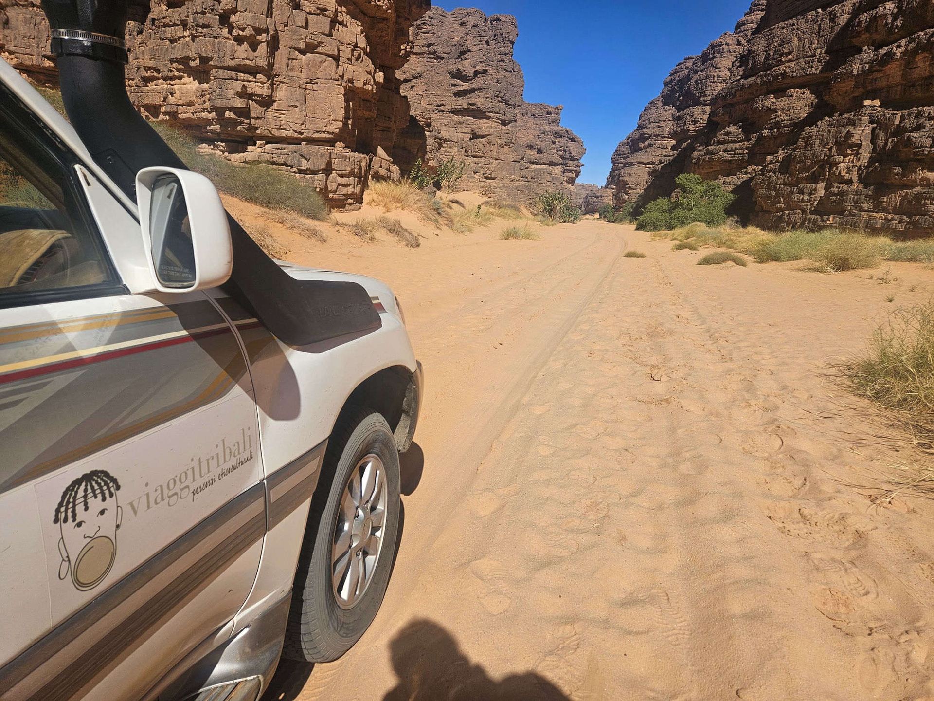 Fuoristrada con logo Viaggitribali attraversa un canyon roccioso nel deserto del Tassili n'Ajjer