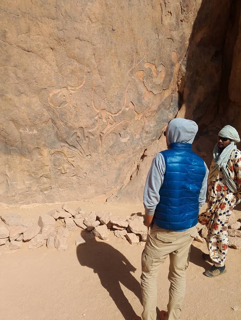 Viaggiatore e guida tuareg osservano la celebre incisione rupestre della Vacca che Piange nel deserto del Tassili n'Ajjer, Algeria