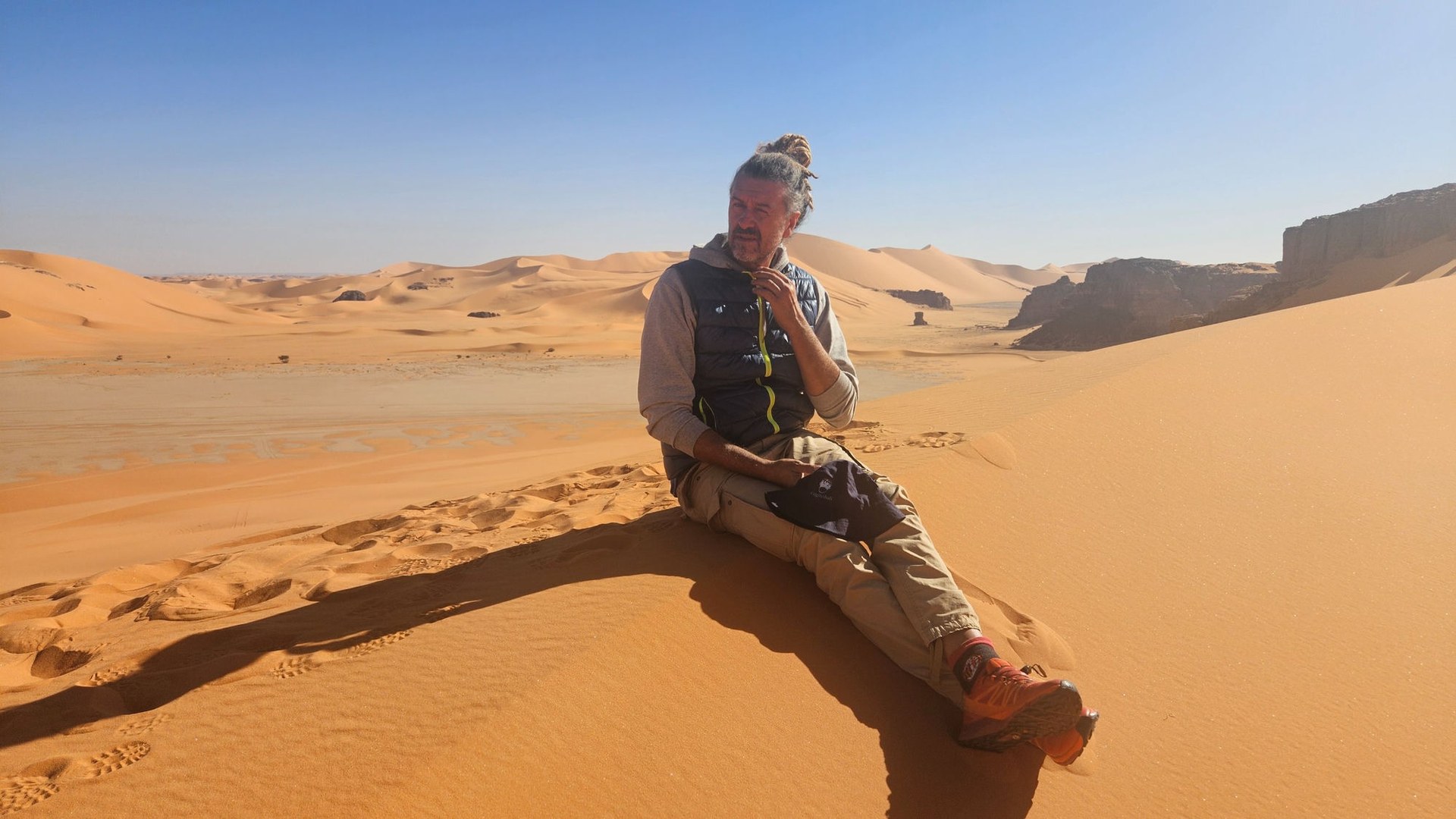 Viaggiatore seduto su una duna durante un tour nel deserto dell'Algeria, sullo sfondo le dune del Tassili n'Ajjer