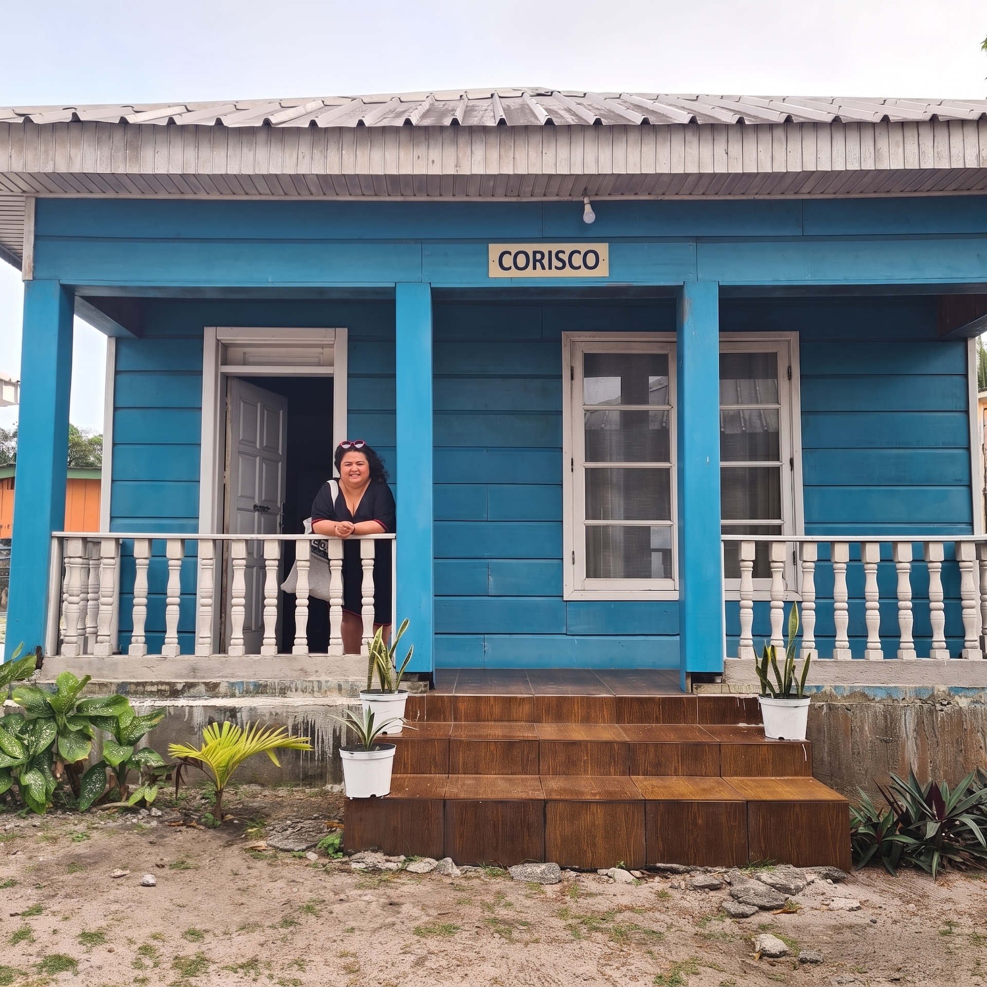 Casa in legno blu con insegna Corisco e una viaggiatrice sorridente affacciata al balcone