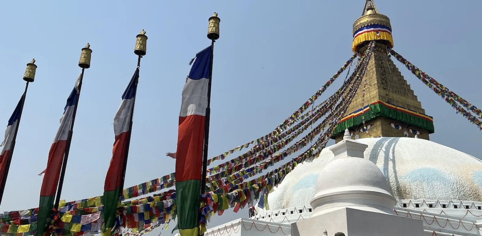 Stupa di Boudhanath con occhi del Buddha, bandiere di preghiera e ruote dorate sotto il cielo limpido di Kathmandu