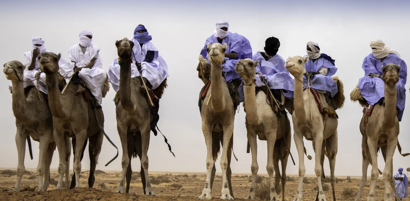Uomini vestiti con abiti tradizionali e turbanti bianchi e blu cavalcano dromedari nel deserto