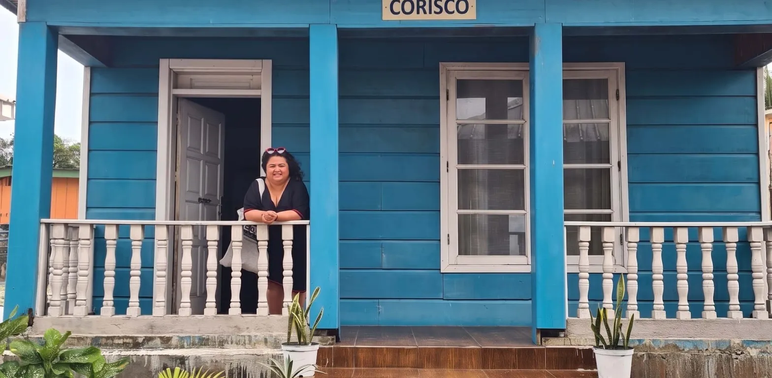 Casa in legno blu con insegna Corisco e una viaggiatrice sorridente affacciata al balcone
