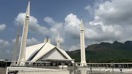 Vasta e moderna Moschea Shah Faisal a Islamabad con quattro minareti e sfondo di colline verdi sotto il cielo azzurro