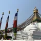 Stupa di Boudhanath con occhi del Buddha, bandiere di preghiera e ruote dorate sotto il cielo limpido di Kathmandu
