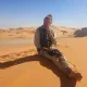 Viaggiatore seduto su una duna durante un tour nel deserto dell'Algeria, sullo sfondo le dune del Tassili n'Ajjer