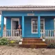 Casa in legno blu con insegna Corisco e una viaggiatrice sorridente affacciata al balcone